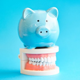Piggy bank atop model teeth representing cost of cosmetic dentistry in Arnold 