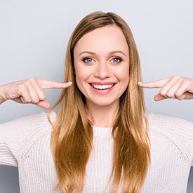 Woman smiling while pointing to her dental crowns in Arnold