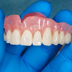 A blue-gloved hand holding an upper denture