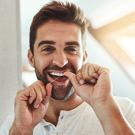 Man smiling while flossing his teeth in bathroom