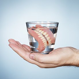 hand holding glass of water with full dentures in it 