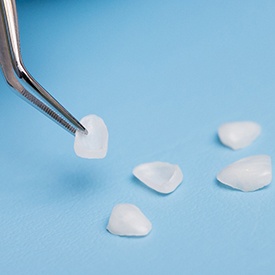 Tweezers holding veneers on blue background 