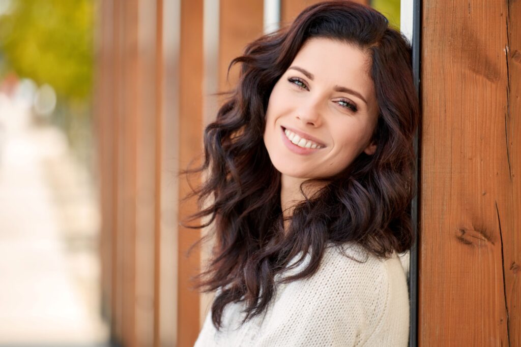 Woman with dark hair leaning against wooden post smiling