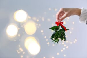 Person holding mistletoe in front of background soft lights.
