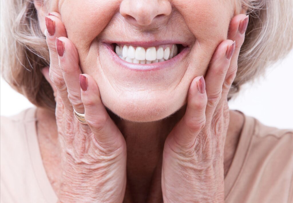 Nose-to-shoulder view of older woman smiling with hands touching cheeks